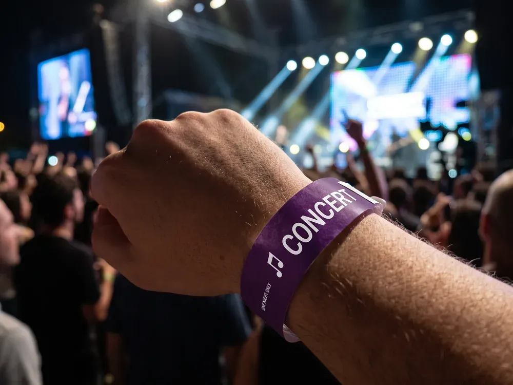 Purple concert wristband worn in front of a lit stage